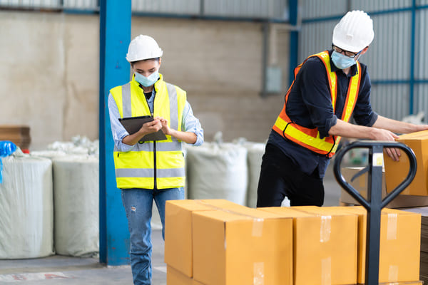 Warehouse workers wearing safety vests, hard hats, and face masks
