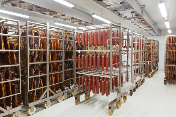 A cold storage room containing carts and racks with hanging meat products