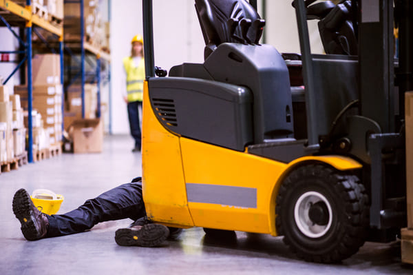 An injured warehouse worker lying down behind an electric forklift