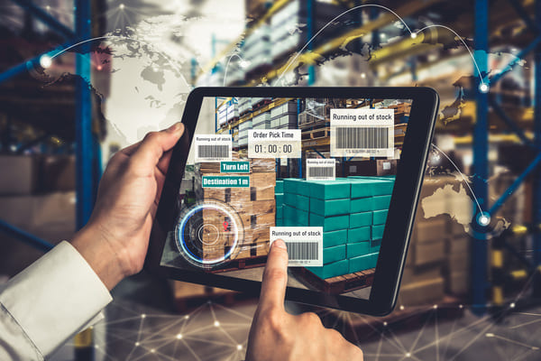 A warehouse worker tapping on a tablet showing inventory levels, shipping times, and order picking times