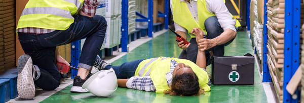 warehouse-workers-rendering-aid-to-injured-coworker Employees in a warehouse rendering first aid to an injured employee