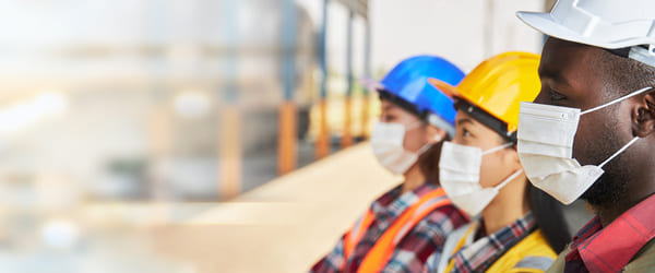 3 warehouse workers wearing face masks lined up looking in the same direction