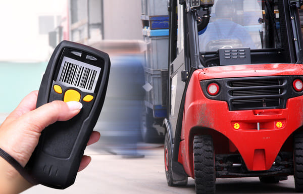 A hand holding an RF scanner pointed at a forklift