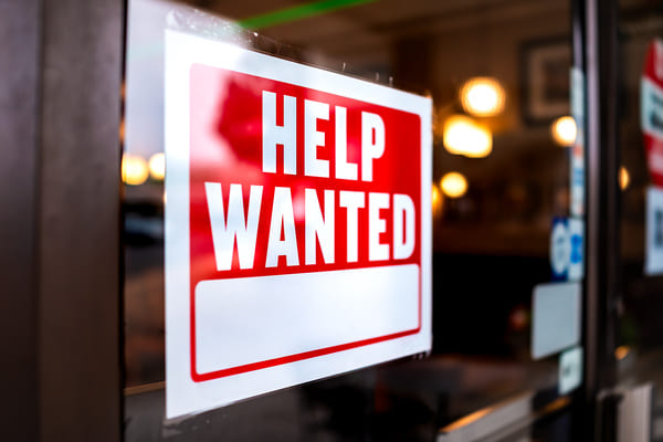 A "help wanted" sign hung in the door of a businesess