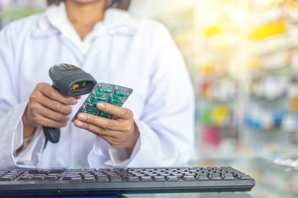 A pharmacist using a handheld RF scanner to scan a package of pills