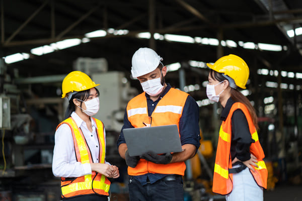 A trio of factory workers looking at a laptop