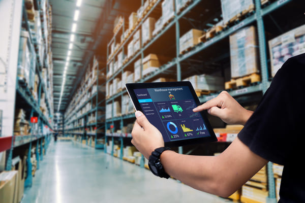 A person standing in a warehouse aisle and tapping on a tablet screen