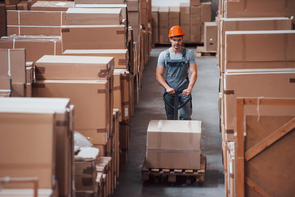 A warehouse worker pushing a pallet jack through an aisle