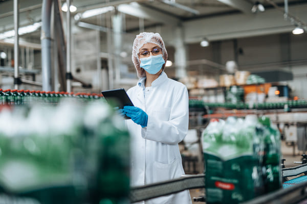 A worker dressed in cleanroom gear inspecting products on a conveyor system in a factory