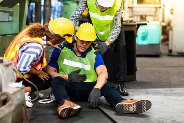 A worker sitting on the floor, injured, and being comforted by their coworkers