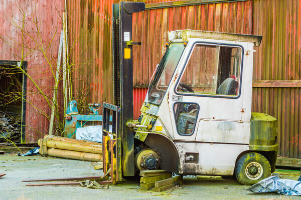 An old forklift missing a tire, kept up on blocks in a yard