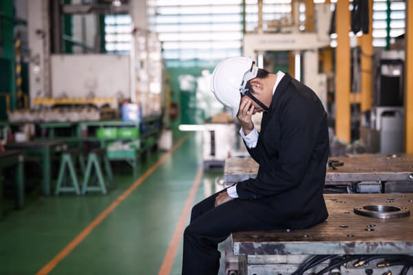 A frustrated executive sitting on a machine in a factory in exasperation