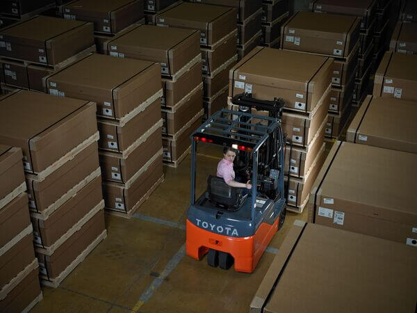 A forklift operator on a Toyota 3-wheel electric forklift moving pallets in a warehouse