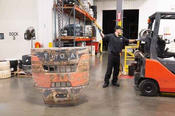 A forklift technician removing a forklift counterweight with a crane