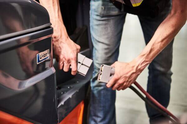 A person plugging in a lithium-ion Toyota forklift battery into a charger