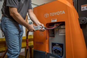 A person plugging a Toyota reach truck lead-acid forklift battery into a charger