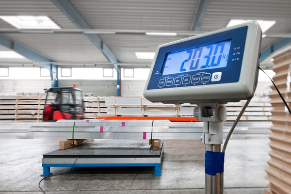 A weight scale in a warehouse with a forklift in the background