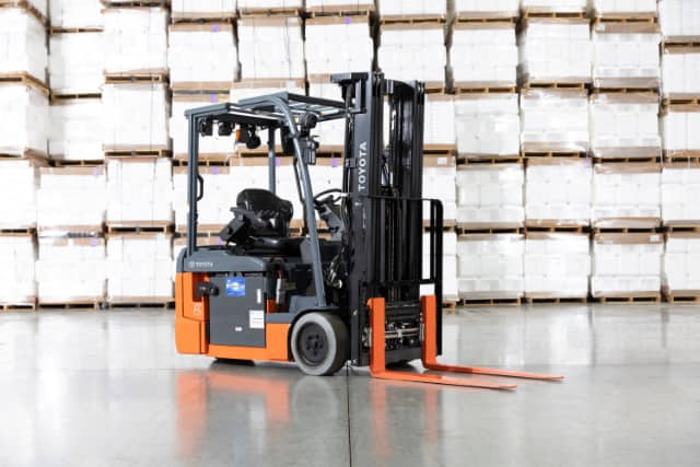 A Toyota 8-series 3-wheel electric sit-down rider forklift parked in front of stacks of pallets