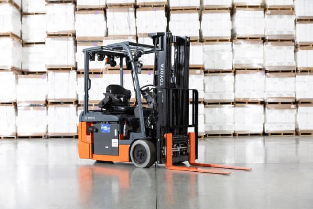 toyota-8-series-3-wheel-electric-sit-down-rider-forklift A Toyota 8-series 3-wheel electric sit-down rider forklift parked in front of stacks of pallets