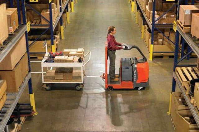 A warehouse worker pulling a cart with a Toyota 8TB50 electric tow tractor