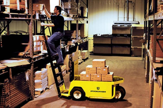 A warehouse worker picking stock on a ladder next to a parked Columbia stockchaser utility vehicle