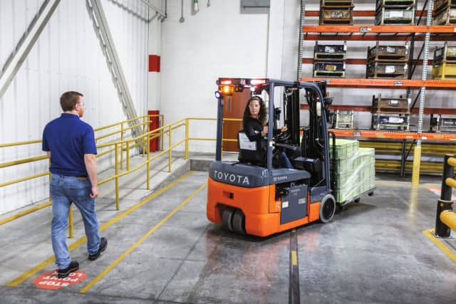 A forklift operator reversing in a Toyota 8FBE18U 3-wheel electric forklift near a pedestrian in a warehouse