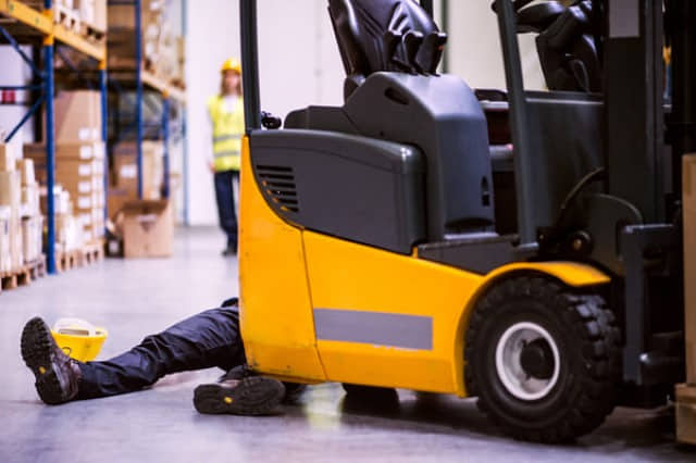 An injured warehouse worker lying on the ground behind a 3-wheel forklift