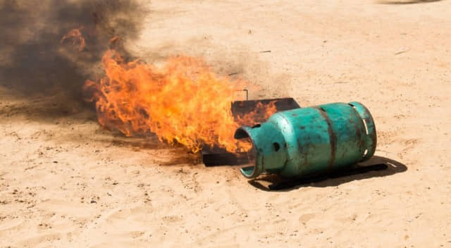 A propane tank laying on the ground on fire