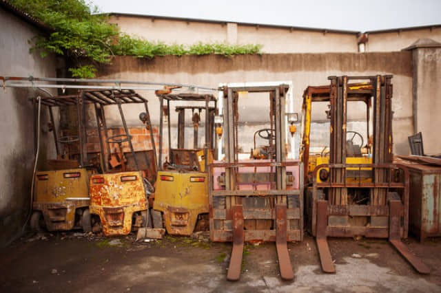 Five scrap forklifts parked outside against wall