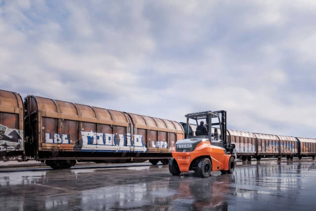 A Toyota electric pneumatic forklift driving outside in a wet railyard