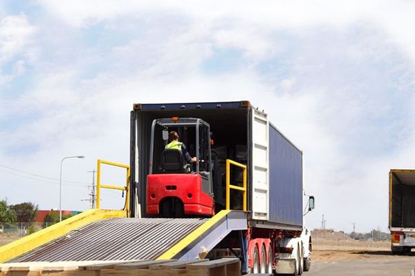 An electric 3-wheel forklift backing down a semi-trailer loading ramp