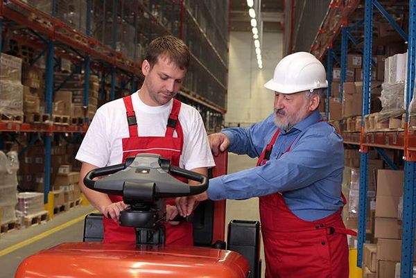 A forklift trainer instructing an operator trainee in a warehouse