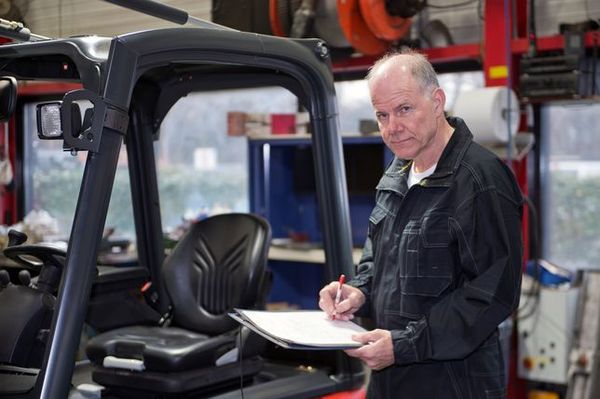 A tire technician recording notes on a clipboard next to a forklift in the shop