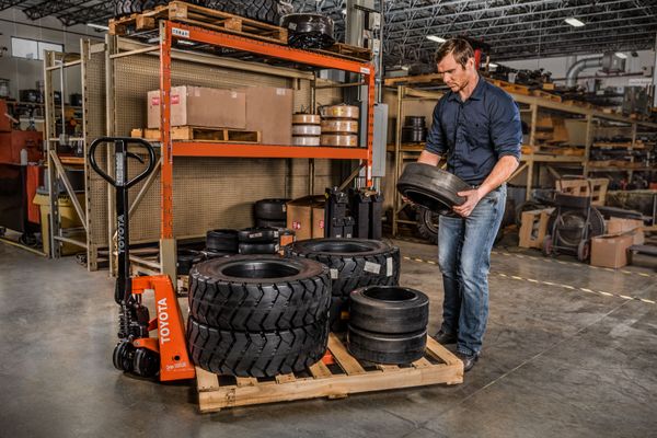 toyota-pallet-jack-forklift-tire-pallet-load-conger-industries A warehouse worker loading forklift tires on a pallet