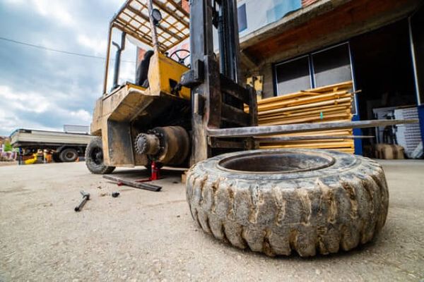 yellow-forklift-tire-off-maintenance-conger-industries A yellow forklift with its tire off undergoing maintenance outside