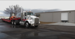 A Conger Industries semi-truck and trailer delivering a refurbished Toyota 7-series pneumatic forklift to a warehouse