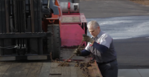 A delivery technician undoing the chain binders securing a refurbished Toyota 7-series pneumatic forklift to a semi-trailer